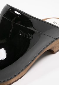 Sabot en cuir noir brillant avec semelle en bois et "Sanita" embossé sur le côté près du bord supérieur cousu.