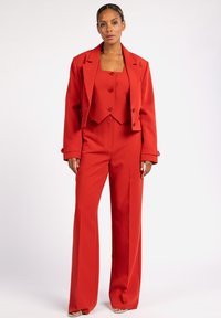 Rode driedelige pak bestaande uit een getailleerde crop top, hoge taillebroek en een oversized blazer. Gladde stof met knoopdetails.