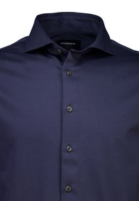 Chemise bleu marine foncé boutonnée, fabriquée dans un tissu à texture lisse. Dotée d'un col pointu et de six boutons sombres sur le devant.