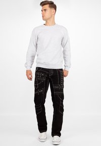 Felpa in cotone grigio chiaro con polsini a costine, abbinata a pantaloni cargo neri con borchie argentate e dettagli di cucitura a contrasto.