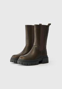 Botas de cuero marrón hasta el tobillo con paneles laterales elásticos, una suela de goma negra gruesa y un acabado suave y texturizado.