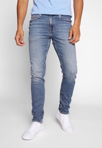 Ljust blå denimjeans med slim fit, urtvättad ton och subtila sömnadsdetaljer. Matchas med vita sneakers för en avslappnad look.