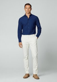 Camicia blu navy con bottoni abbinata a pantaloni bianchi, con taglio dritto e scarpe beige; tessuto morbido e design classico.