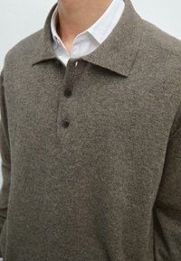 Hnědý pletený polokošile s plochým límcem, vybavená třemi černými knoflíky, texturovanou látkou a vrstvená přes bílou pruhovanou košili.