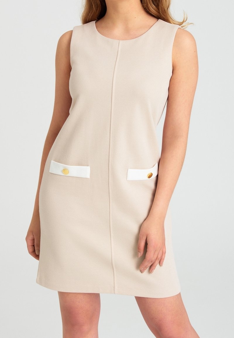 Robe beige sans manches à coupe droite, avec des rabats de poche blancs ornés de boutons dorés sur les hanches avant.