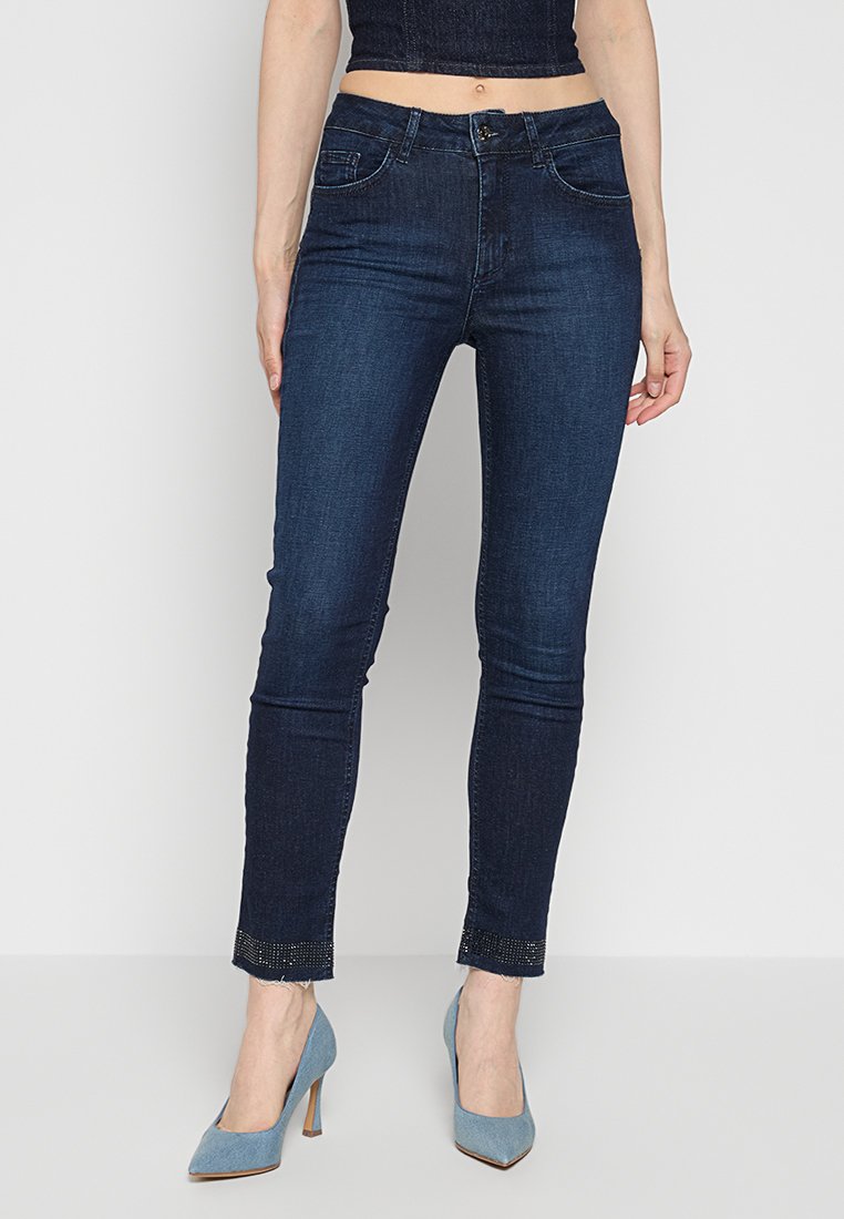Jeans skinny blu scuro realizzati in denim, con vita a media altezza, sottili decorazioni all'orlo e una trama liscia.