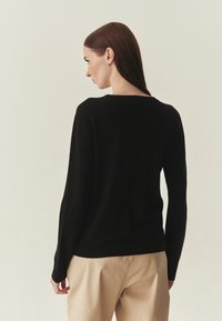 Pull noir à col rond, manches longues et ourlet côtelé. Texture douce, silhouette ajustée et design minimaliste sans motifs visibles.