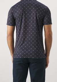 Marinblå t-shirt med kort ärm, prydd med ett geometriskt mönster och tillverkad i mjukt tyg med en figurnära design. Detaljerna inkluderar små vita accenter genom hela tröjan.