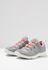 Sneaker in mesh grigio e sintetico con accenti e lacci arancioni, suola bianca, collo imbottito e dettagli a fantasia sulla parte superiore.