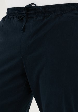 Pantaloni navy blue con vita elastica e coulisse, caratterizzati da una texture liscia e una tasca laterale. Nessun motivo o decorazione visibile.