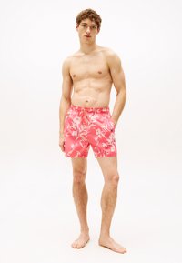 Bañador rosa con un patrón floral, cintura elástica con cordón ajustable y bolsillos laterales. El material parece ligero.