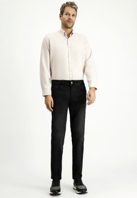 Jeans in denim nero abbinati a una camicia a maniche lunghe di un rosa chiaro. I jeans presentano una chiusura con bottone e tasche laterali, con una texture liscia.