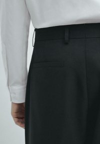 Schwarze maßgeschneiderte Hosen mit einem eleganten Design, einer Gesäßtasche und einer glatten Textur, kombiniert mit einem weißen Langarmhemd.