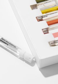 Duftproben-Set mit klaren Glasfläschchen in verschiedenen Farbtönen, präsentiert in einer weißen rechteckigen Schachtel mit bedrucktem Etikett.