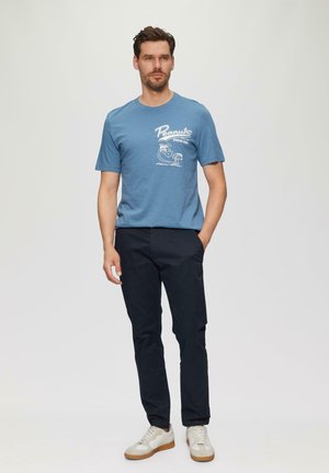 Blauwe katoenen t-shirt met een witte "Peanuts" grafische print, gecombineerd met zwarte broek en lichtgekleurde sneakers.
