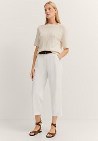 Beige knit sweater, white pleated trousers, and brown ankle strap sandals. Sweater has short sleeves, trousers are cropped, smooth fabric.