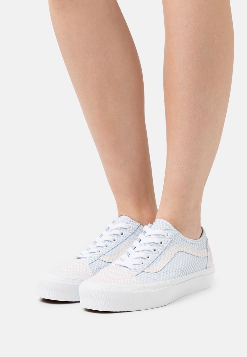 Baskets blanches avec une tige texturée aux motifs bleu clair et rose, dotées de lacets blancs et d'une semelle en caoutchouc.