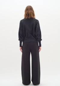 Grå oversized tröja med neddragna axlar, kombinerad med svarta vida byxor, som har en mjuk textur och minimalistisk design.