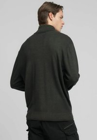 Suéter tejido de color verde oscuro con cuello alto, dobladillo acanalado y mangas largas, con un acabado texturizado y un ajuste holgado.