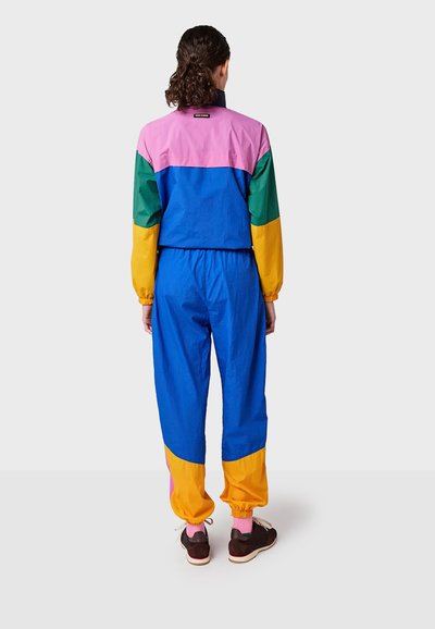 Kleurrijke trainingspak met een ontwerp in kleurblokken in roze, groen, blauw en geel, voorzien van elastische manchetten en een elastische tailleband, gemaakt van lichtgewicht materiaal.
