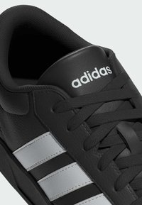 Čierna kožená teniska s tromi bielymi pruhmi, čiernymi šnúrkami a čiernym jazýčkom s bielym logom „adidas“.