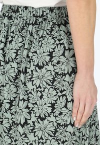 Jupe florale avec un motif noir et vert clair, dotée d'une taille élastique et d'une texture de tissu douce, idéale pour un style décontracté.