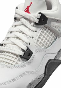 Sneaker blanche avec tige en cuir, panneaux en maille et accents noirs. Les détails notables incluent un logo rouge et une semelle intermédiaire grise mouchetée.