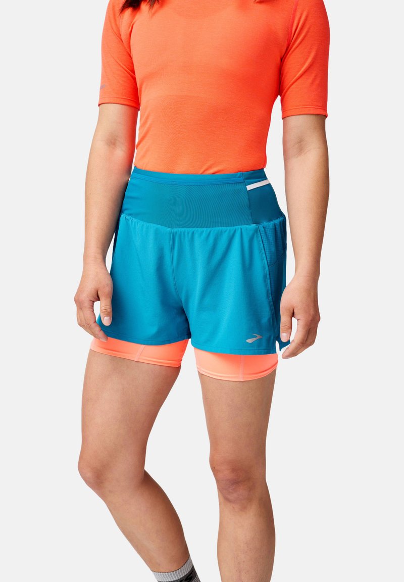 Shorts de course turquoise avec une taille élastique, superposés à des shorts de compression orange vif. Comprend des accents réfléchissants.