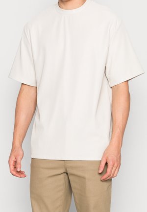 Lichtbeige shirt met korte mouwen met geribbelde textuur, voorzien van een ronde halslijn en een losse pasvorm. Gecombineerd met kaki broek.