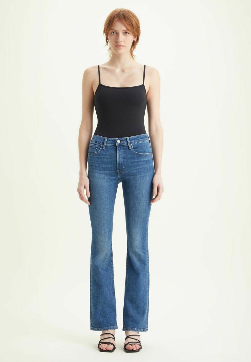 Body nero e jeans in denim azzurro chiaro a zampa d'elefante. I jeans presentano una vita alta e una consistenza morbida. Sono indossate delle sandali neri con cinturini.