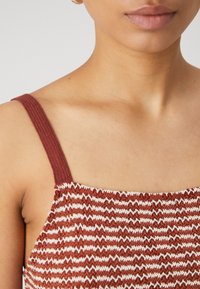 Haut tricoté marron et blanc avec un col carré, doté de larges bretelles texturées et d'un motif en zigzag sur l'ensemble du tissu.