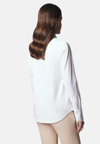 Biała koszula z długim rękawem, o zaokrąglonym dole i zapinanych mankietach, wykonana z gładkiego materiału. Posiada klasyczny kołnierzyk i dopasowany krój.