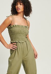 Haut smocké vert olive avec des volants et des bretelles à nouer ajustables. Accompagné d'un pantalon assorti à coupe ample pour un look coordonné.