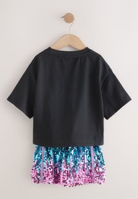 Schwarzes kurzärmeliges Oberteil mit einem Paillettenrock, der einen Farbverlauf von Blau zu Pink zeigt. Strukturierte Pailletten und genähte Akzente vervollständigen das Design.