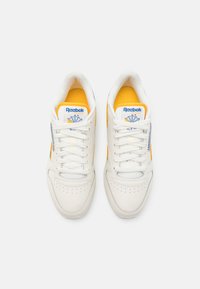 Białe sneakersy z żółtymi akcentami i niebieskim logo, z gładką skórzaną cholewką, perforowanymi palcami i tradycyjnym sznurowaniem.