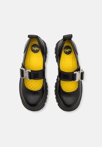 Mustad nahast kingad kollase perforatsiooniga sisemusega. Omab rihma hõbedase klambriga ja tugevat talda parema haarde jaoks.