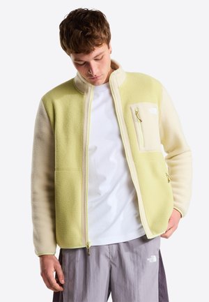 Vaaleankeltainen ja kermaisen sävyinen fleecetakki. Siinä on vetoketjullinen rintatasku, kaksi sivutaskua ja kontrastiset tekstuurit. Vetoketjukiinnitys.