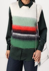 Sweter bez rękawów z dzianiny w poziome paski w kolorach zielonym, czerwonym, czarnym i kremowym, nałożony na ciemnozieloną koszulę z kołnierzykiem, w zestawie z srebną torbą.