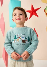 Pull en tricot bleu clair avec des animaux de la forêt et des arbres brodés sur le devant. Le texte "Feliz Navidad" est écrit en noir. Poignets côtelés.