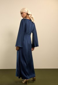 Pikk, tumesinine satiinist kleit, millel on laiad varrukad ja tagumine lukk. Kandmisena helepealne pearätt ja kuldsed kontsad.