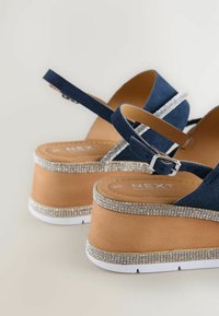 Sinine sametist platvormsandaalid tan värvi alusel ja valge välispinnaga. Kaunistatud rhinestone'idega ümber talla, varustatud klamberrihmaga.