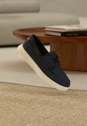 Navy canvas schoen met witte rubberen zool, voorzien van een ronde neus, veters en gestikte details. Lichtgewicht en casual ontwerp.