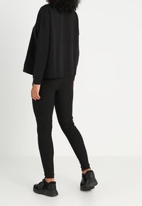 Svart långärmad sweatshirt i kombination med svarta och vita randiga leggings. Leggingsen är figurnära och båda plaggen har en enkel design.