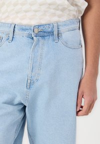 Light blue denim jeans with a high waist, five pockets, metal button closure, and contrast stitching. Smooth texture with a slightly worn look.