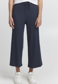 Navy ribbed knit wide-leg pants with a drawstring waistband. Styled with white sneakers and a simple white top.