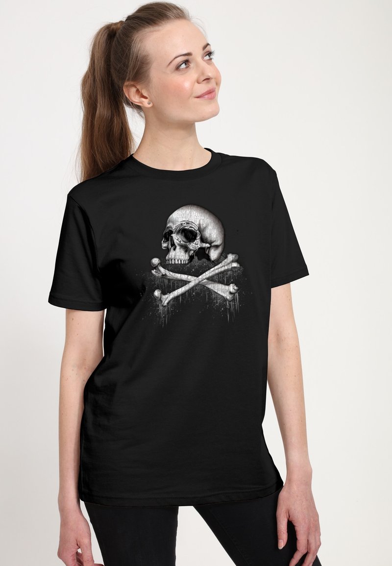Svart t-shirt i bomull, med en framträdande grafik av ett skalle och korslagda ben i grått och vitt, mot en texturerad bakgrund.