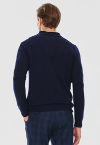 Granatowy, długirekawowy sweter typu pullover z prążkowanym dołem i kołnierzem; wykonany z miękkiego materiału. W zestawie z spodniami w kratę.