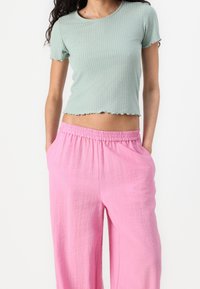 Haut court côtelé vert menthe avec un ourlet festonné, associé à un pantalon rose ample avec une taille élastique et un tissu texturé.