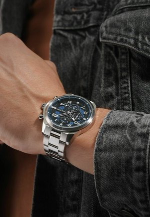 Stainless steel watch with a blue dial, silver numbers, and sub-dials. Features a linked bracelet and a round, slightly convex case.