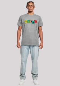 Gray cotton t-shirt featuring colored block designs with chemical symbols in yellow, green, blue, pink, and red, paired with light jeans and white sneakers.